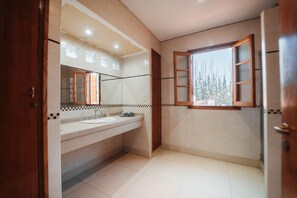 Un baño con un espejo grande, dos lavamanos y una ventana con vistas a árboles.