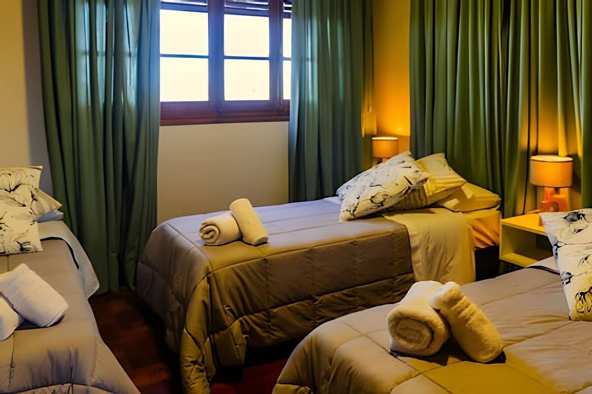 Une chambre d’hôtel avec deux lits, chacun agrémenté de serviettes pliées, de rideaux verts et d’une fenêtre laissant entrer la lumière naturelle.