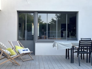 En terrasse med et bord, stole, et vindue og en liggestol med puder.