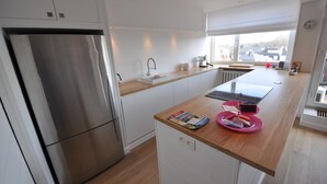 Een moderne keuken met een roestvrijstalen koelkast, witte kastjes, een houten aanrechtblad en een raam met uitzicht.