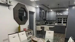 A modern kitchen with dark cabinets, a central island, and a dining area with a glass table and white chairs. - Cypress Suites (Roseau)