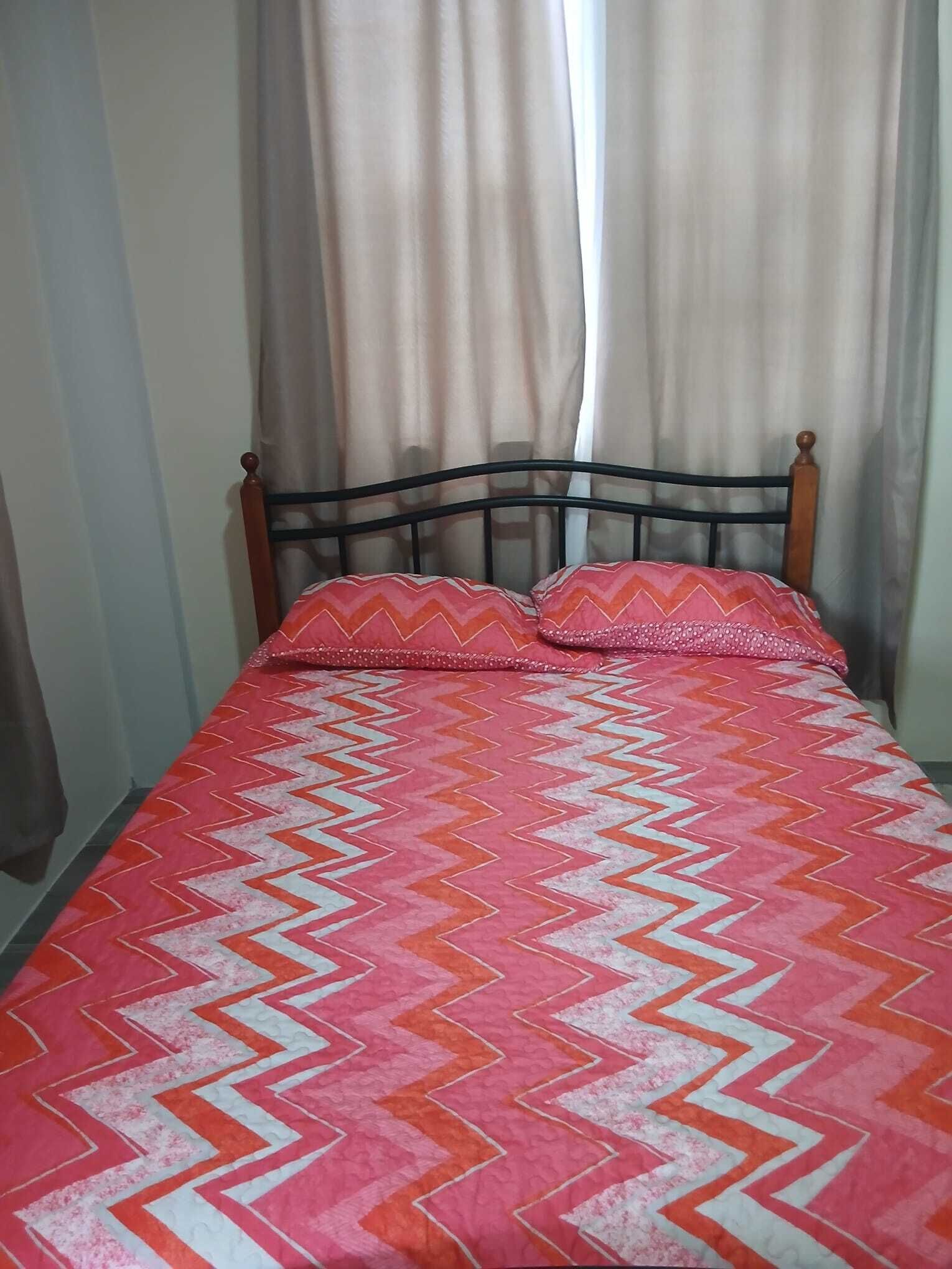 Una cama con una colcha estampada y dos almohadas, un cabecero de madera y una cortina.