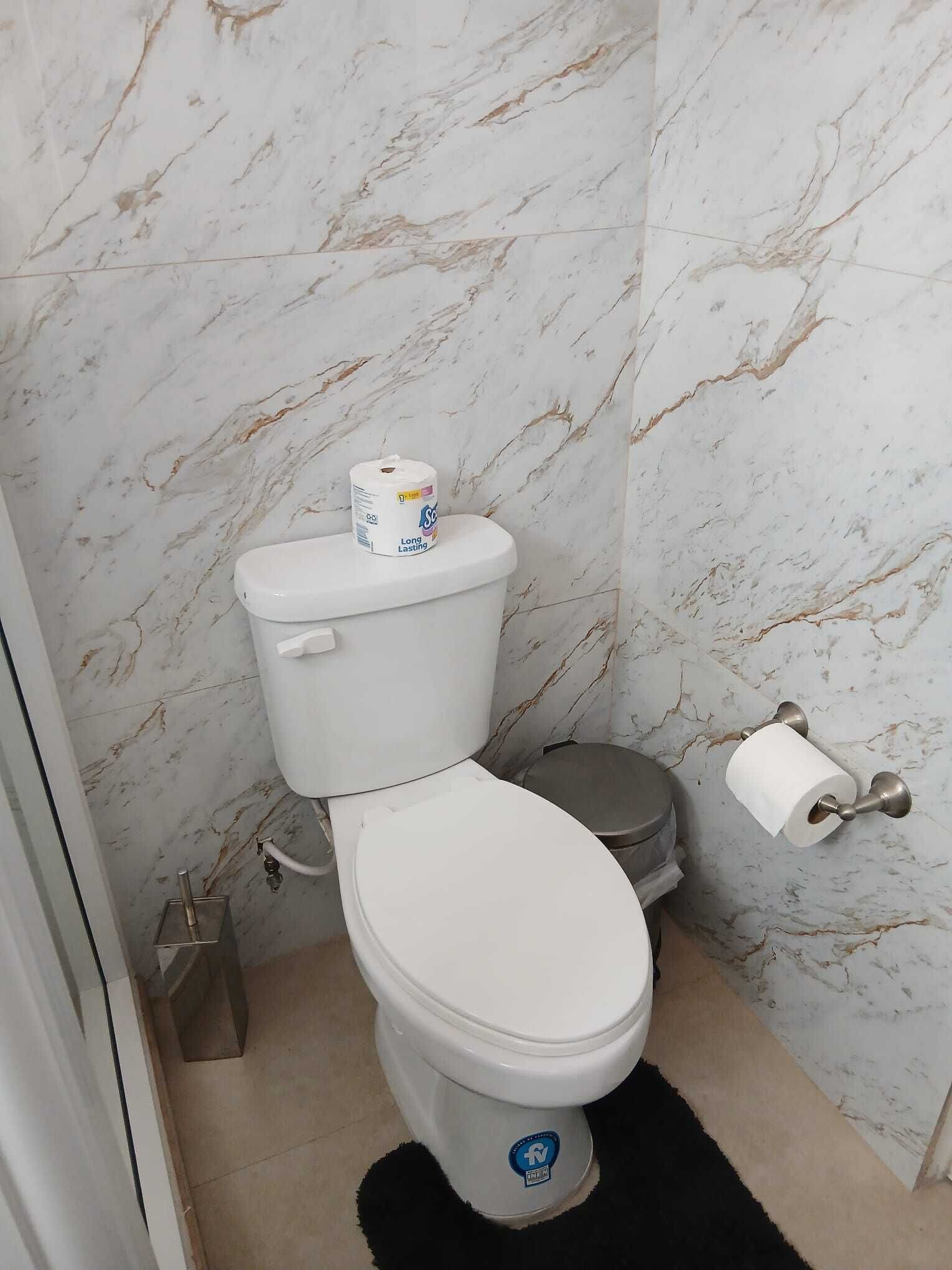 Une salle de bain avec des toilettes blanches, des murs en marbre et un tapis noir.