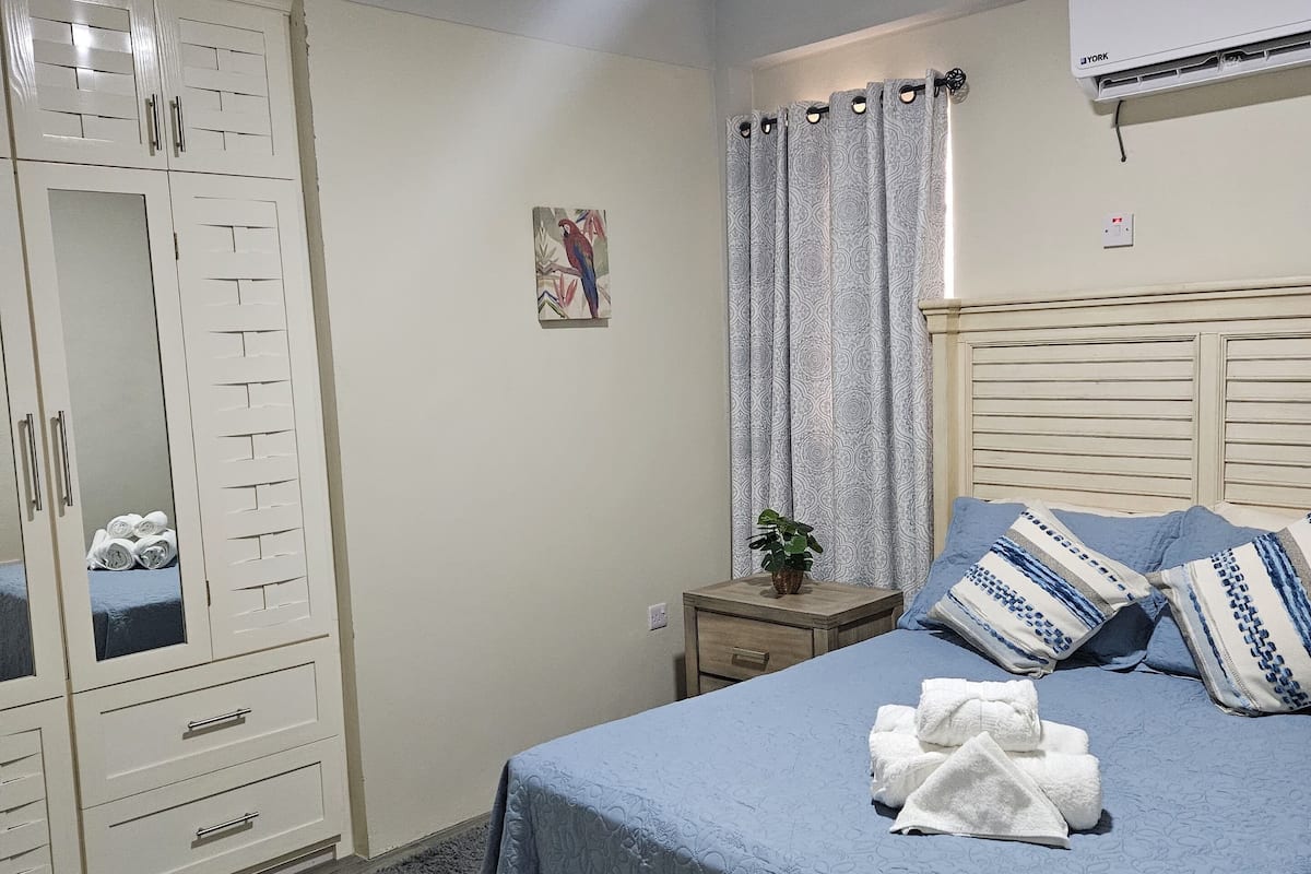 A bedroom with a bed, a wardrobe, a nightstand, and a window with curtains.