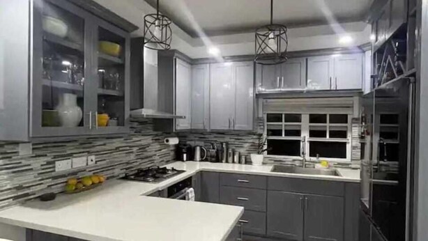 A modern kitchen with grey cabinets, a central island with bar stools, and pendant lighting. - Cypress Suites (Roseau)