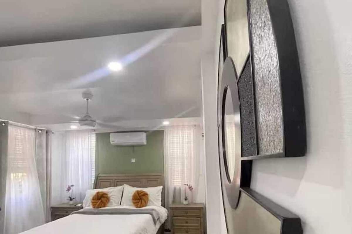 A bedroom with a bed, wooden flooring, a ceiling fan, and a wall-mounted air conditioning unit.