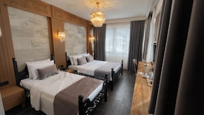 A hotel room with two beds, a wooden headboard, a chandelier, a wooden desk, and a large window with curtains. - TURİSTİK PALAS OTEL (Diyarbakir)