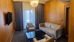 A modern hotel room with a sofa, armchairs, a glass coffee table, and a chandelier. - TURİSTİK PALAS OTEL (Diyarbakir)