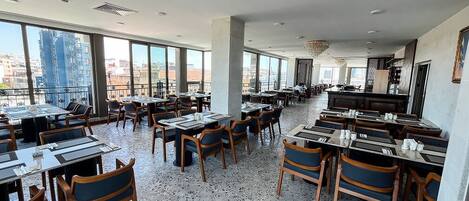 A spacious restaurant with high ceilings, large windows, and a terrazzo floor.