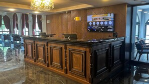 A reception area with a wooden counter, a television mounted on the wall, and a view of the outside through large windows.
