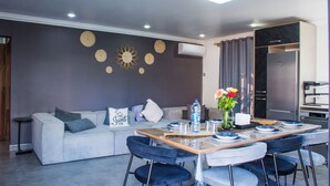 A modern living room with a grey sofa, blue chairs, a dining table set with plates and a vase of flowers. - Fazz Boutique Villa-private pool (Grand Baie)