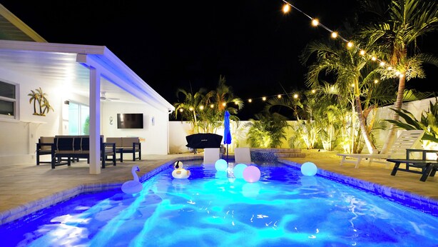 A swimming pool with a swan float and colorful balls, surrounded by palm trees and string lights. - Island 3 bed 3 bath heated pool golf cart kayaks (Indian Rocks Beach)