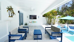 A covered patio with outdoor seating, a television, and a pool area. - Island 3 bed 3 bath heated pool golf cart kayaks (Indian Rocks Beach)