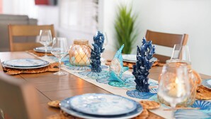 A dining table set with blue plates, clear glasses, and decorative items including a fish sculpture and a candle in a glass jar. - Island 3 bed 3 bath heated pool golf cart kayaks (Indian Rocks Beach)