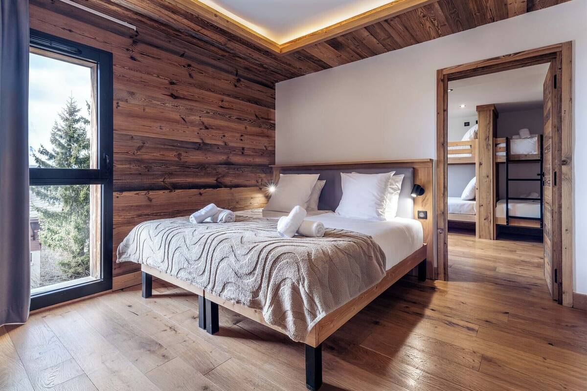 Ein modernes Schlafzimmer mit Holzboden, einem großen Bett mit weißer Bettwäsche und Blick durch ein großes Fenster.