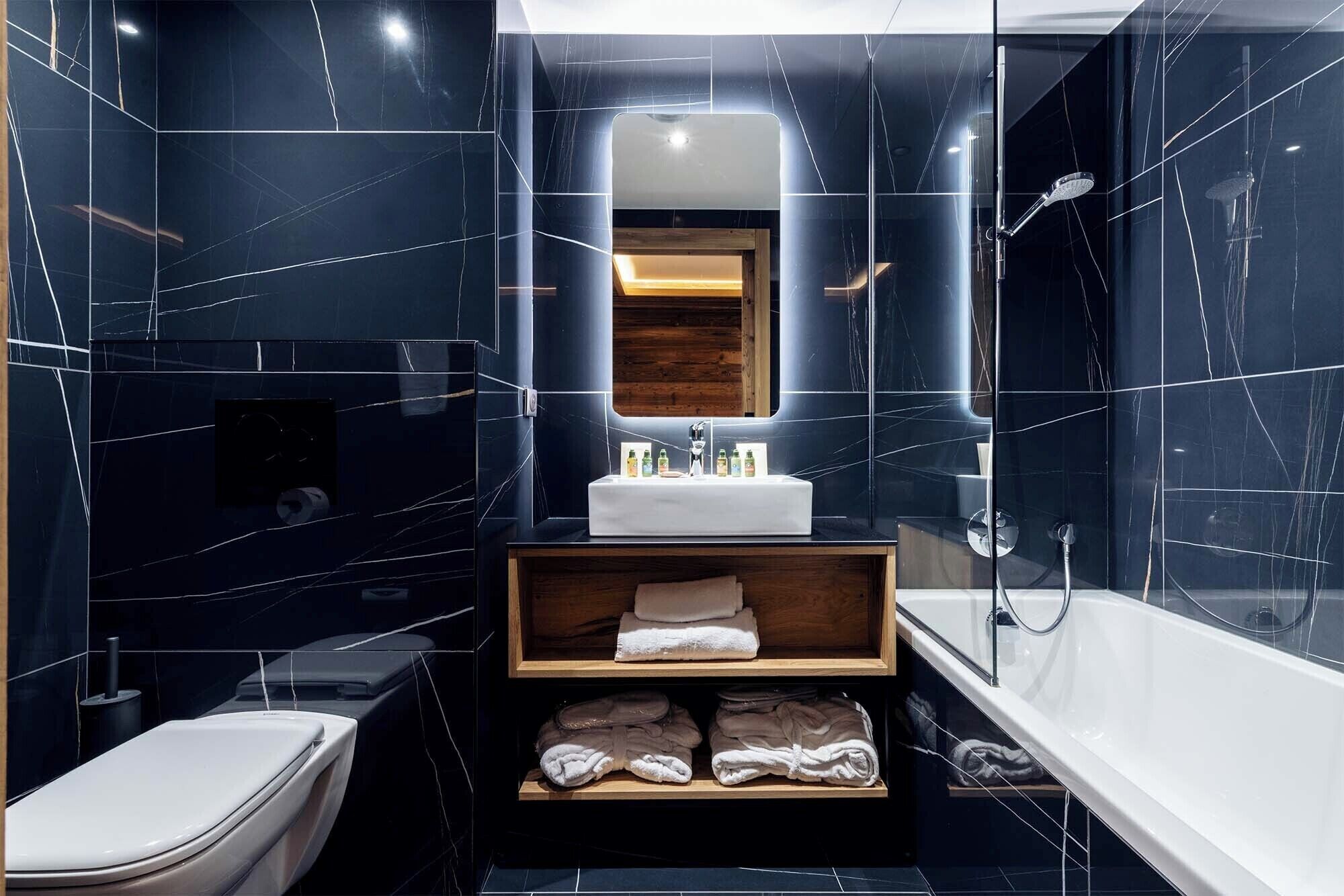 A modern bathroom with dark marble walls, a white sink, a mirror, a shower, and a toilet.