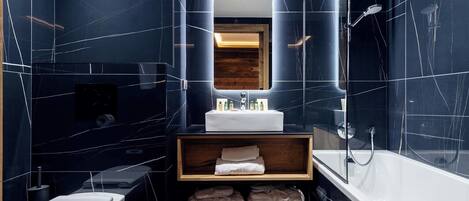 A modern bathroom with dark marble walls, a white sink, a mirror, a shower, and a toilet.
