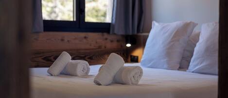 Una cama bien tendida con sábanas y almohadas blancas, un cabecero de madera y una ventana con cortinas.