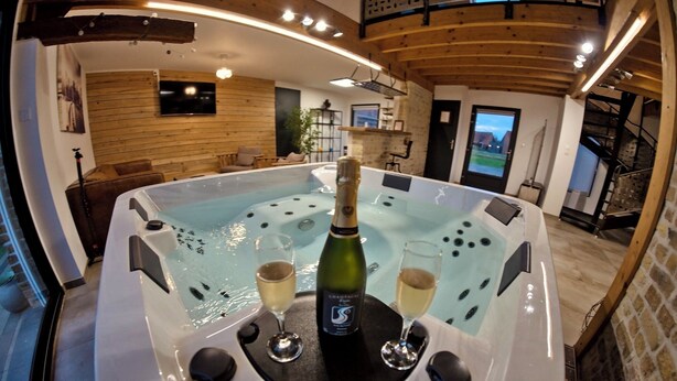 A hot tub with two glasses of champagne and a bottle in the center, surrounded by wooden walls and a TV on the wall. - Loft Terre Jacuzzi and sauna Gravelines (Gravelines)