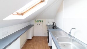 Een compacte keuken met dakraam, witte kastjes, een inbouwoven en een RVS spoelbak.