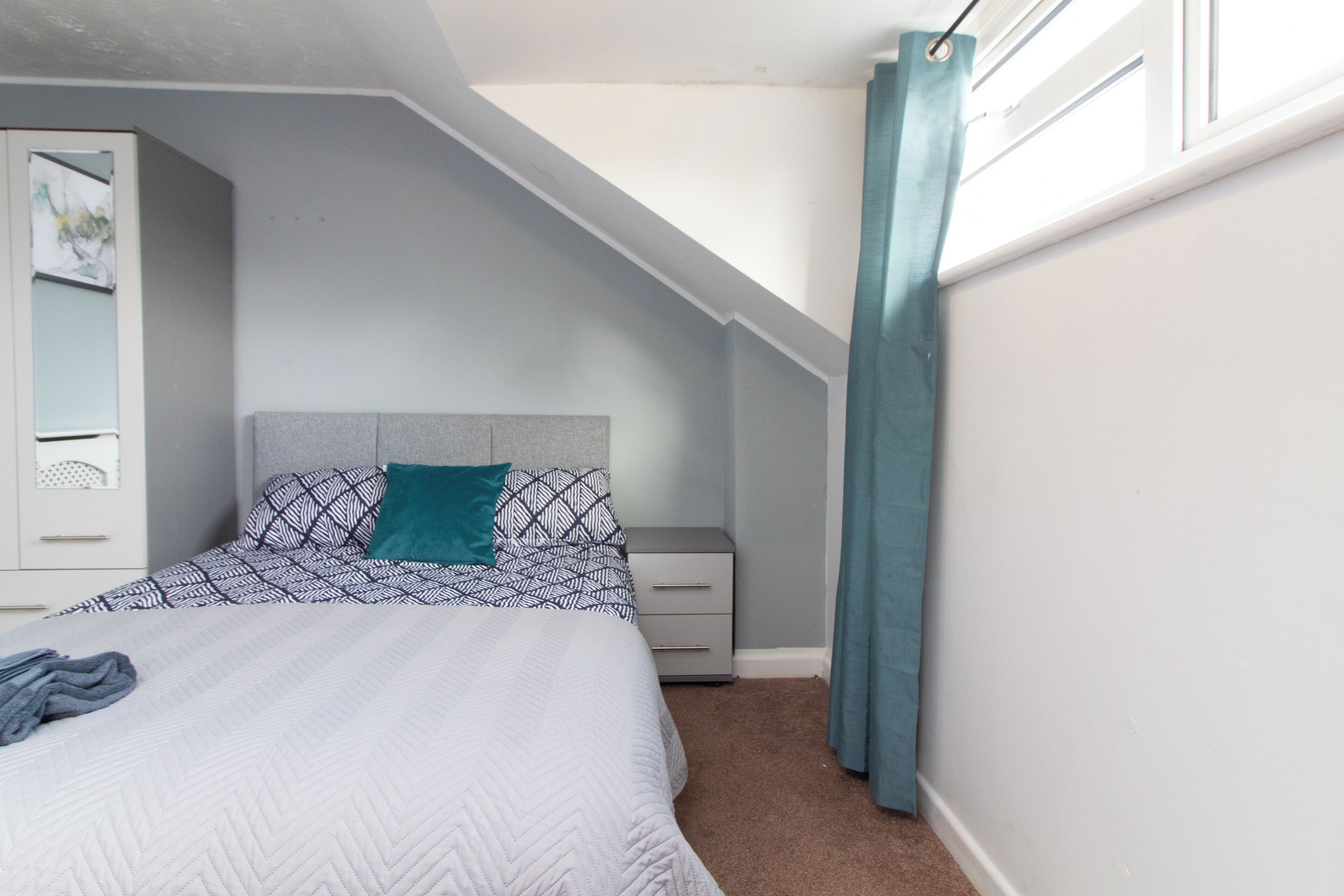 A bedroom with a bed, a nightstand, a dresser, and a window with curtains.