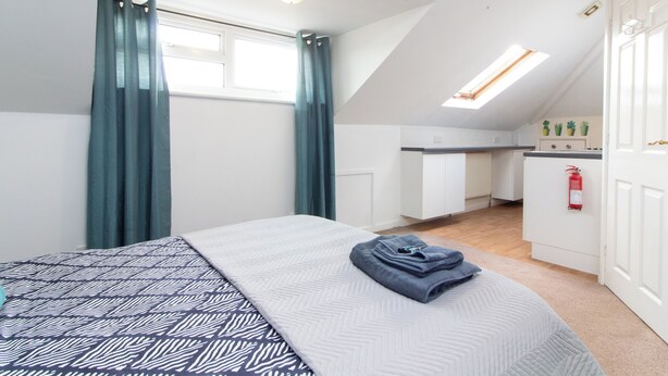 Een slaapkamer met een bed, een raam met gordijnen, een kitchenette en een plafondlamp.