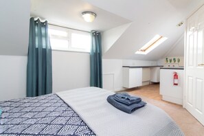 A bedroom with a bed, a window with curtains, a kitchenette, and a ceiling light. - Thornbury Guest House Room 7 (Southampton)