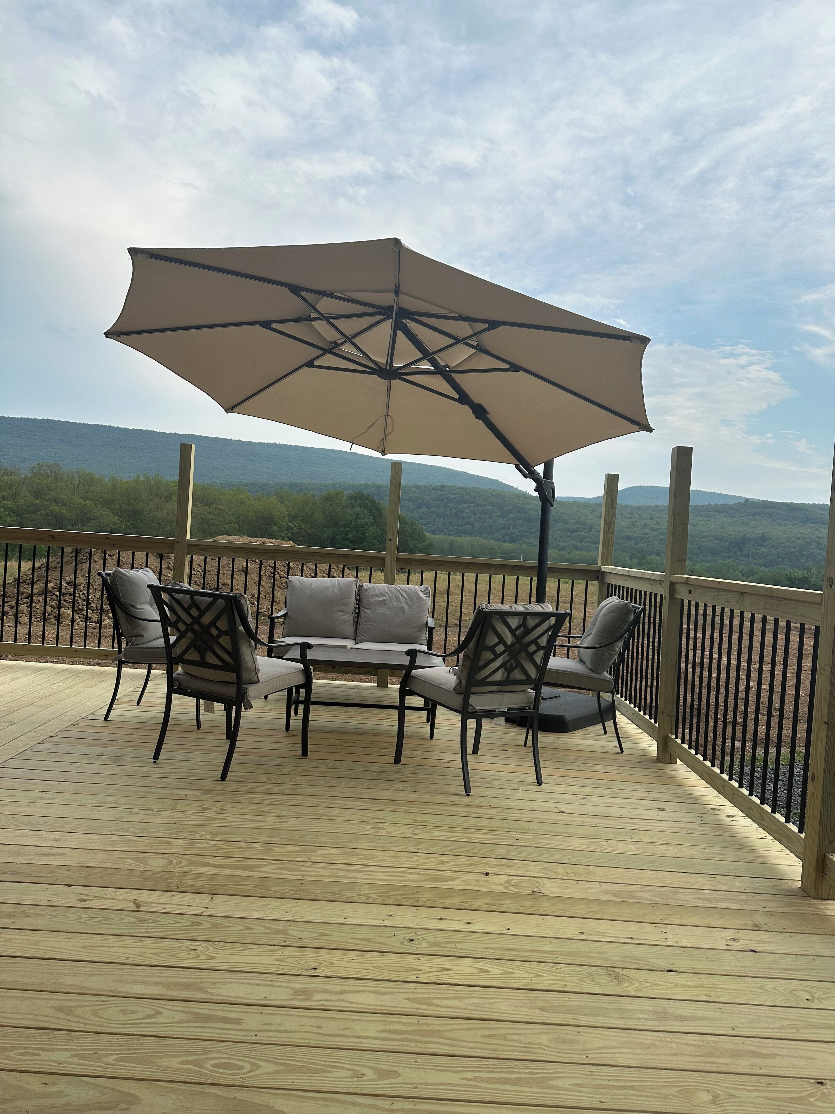 Een houten terras met tuinmeubilair, waaronder een tafel en stoelen, en een grote parasol die schaduw biedt.