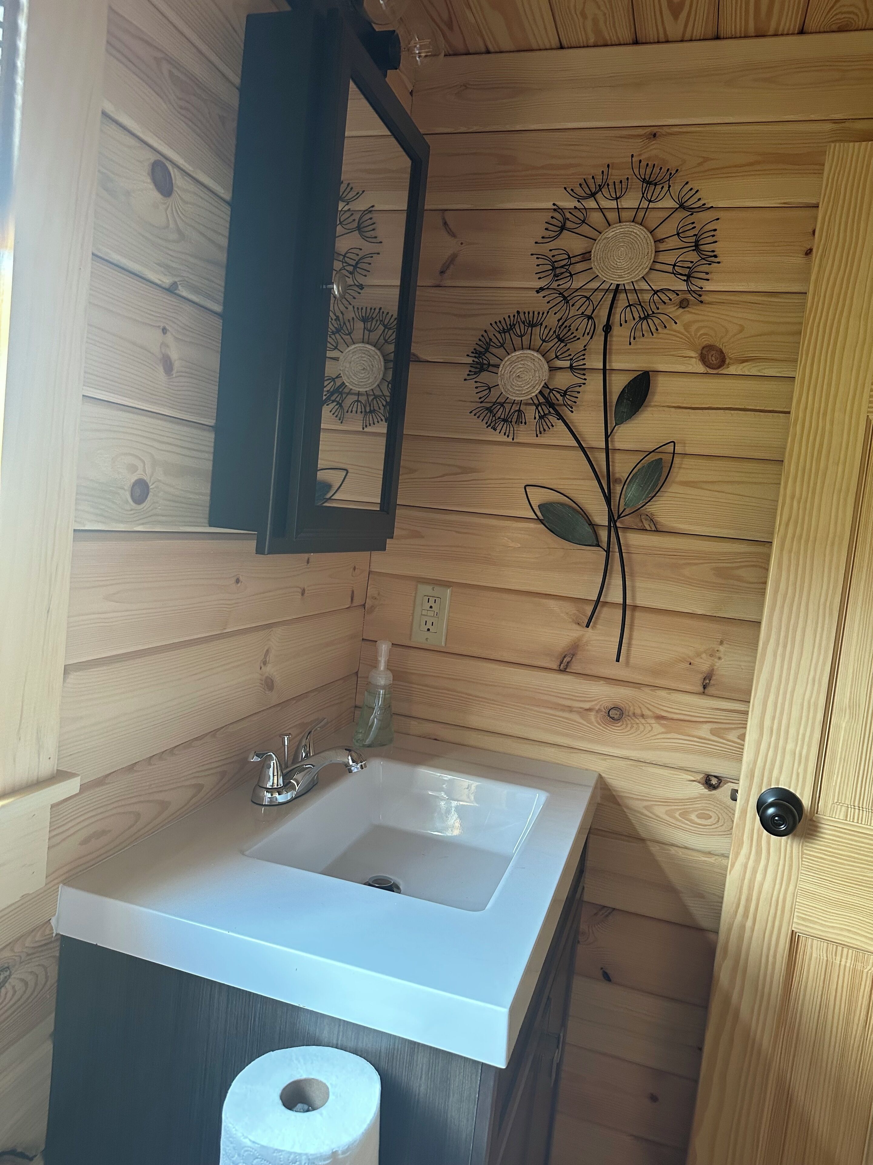 A bathroom with a wooden interior, a white sink, a mirror, and a decorative wall piece.