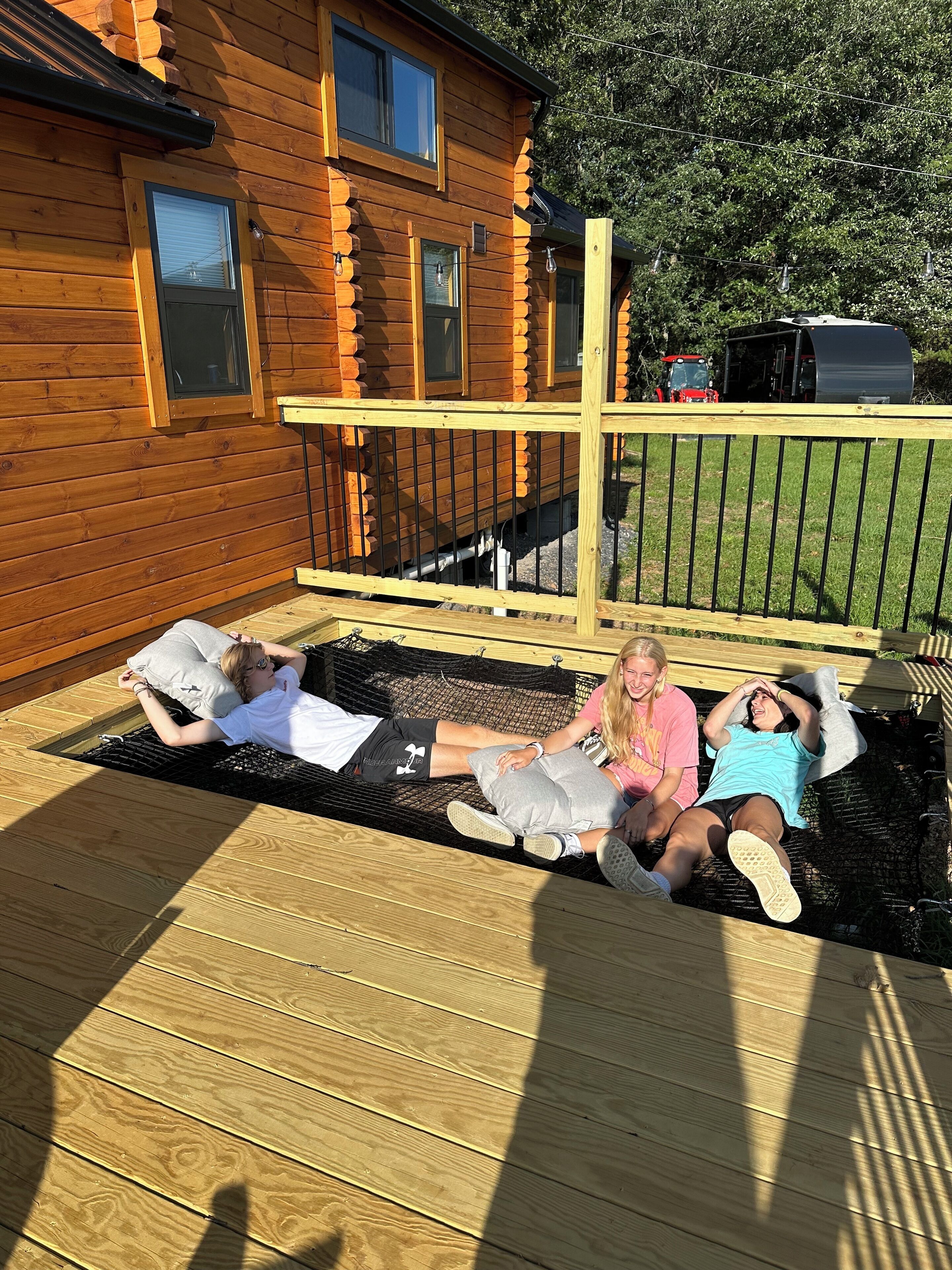 Eine Holzterrasse mit einer Hängematte und einem Holzhaus im Hintergrund.