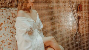 Una persona sentada en un banco de azulejos en una habitación con zona de ducha.