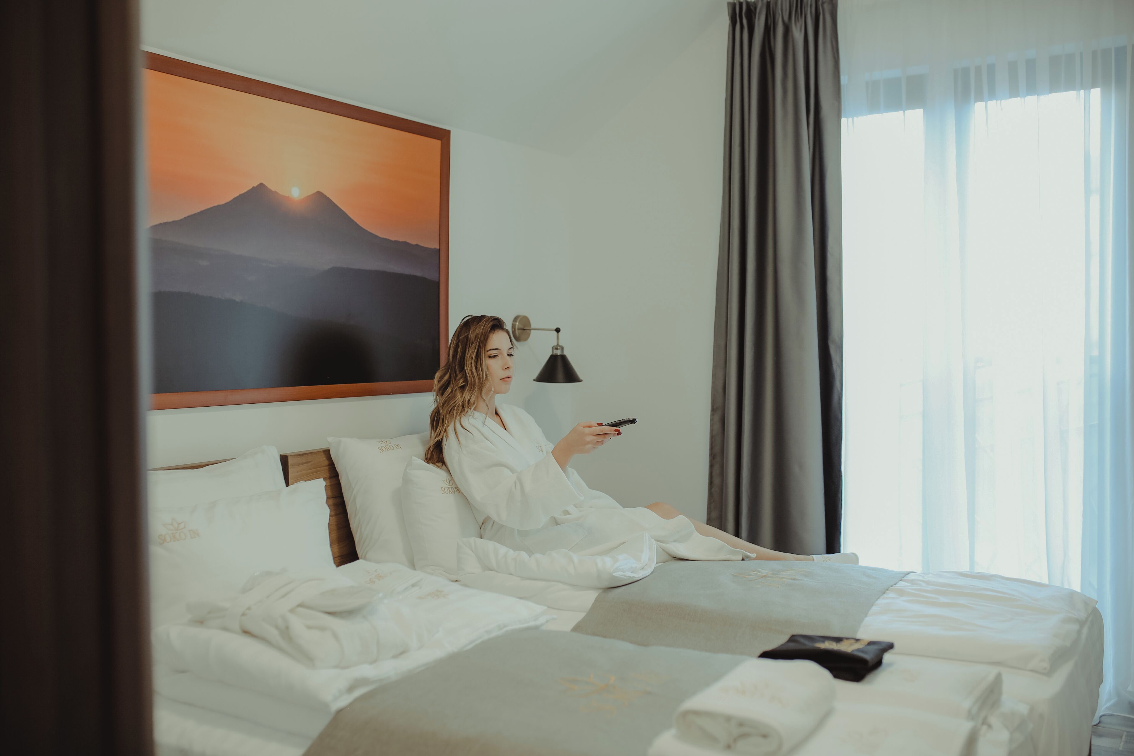 Una habitación de hotel con una cama, una lámpara de noche y un cuadro de un paisaje de montaña.