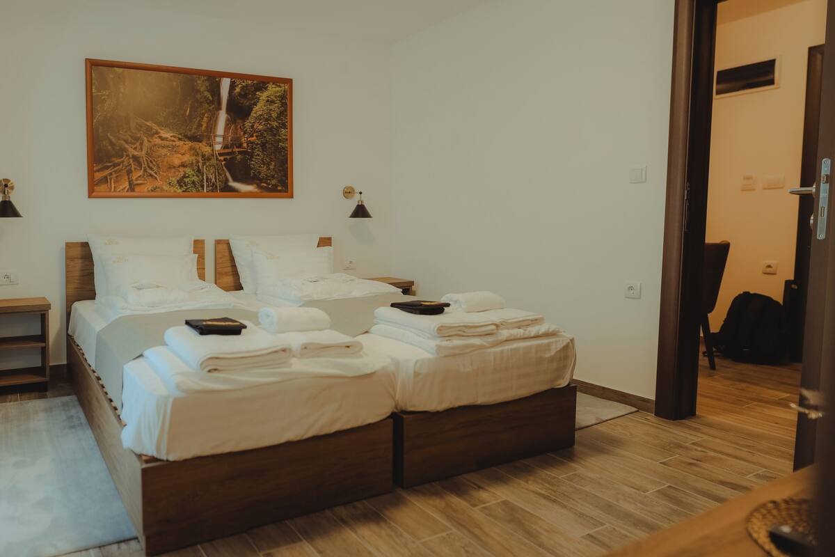 A bedroom with a wooden bed, white linens, a painting of a waterfall, and two bedside lamps.