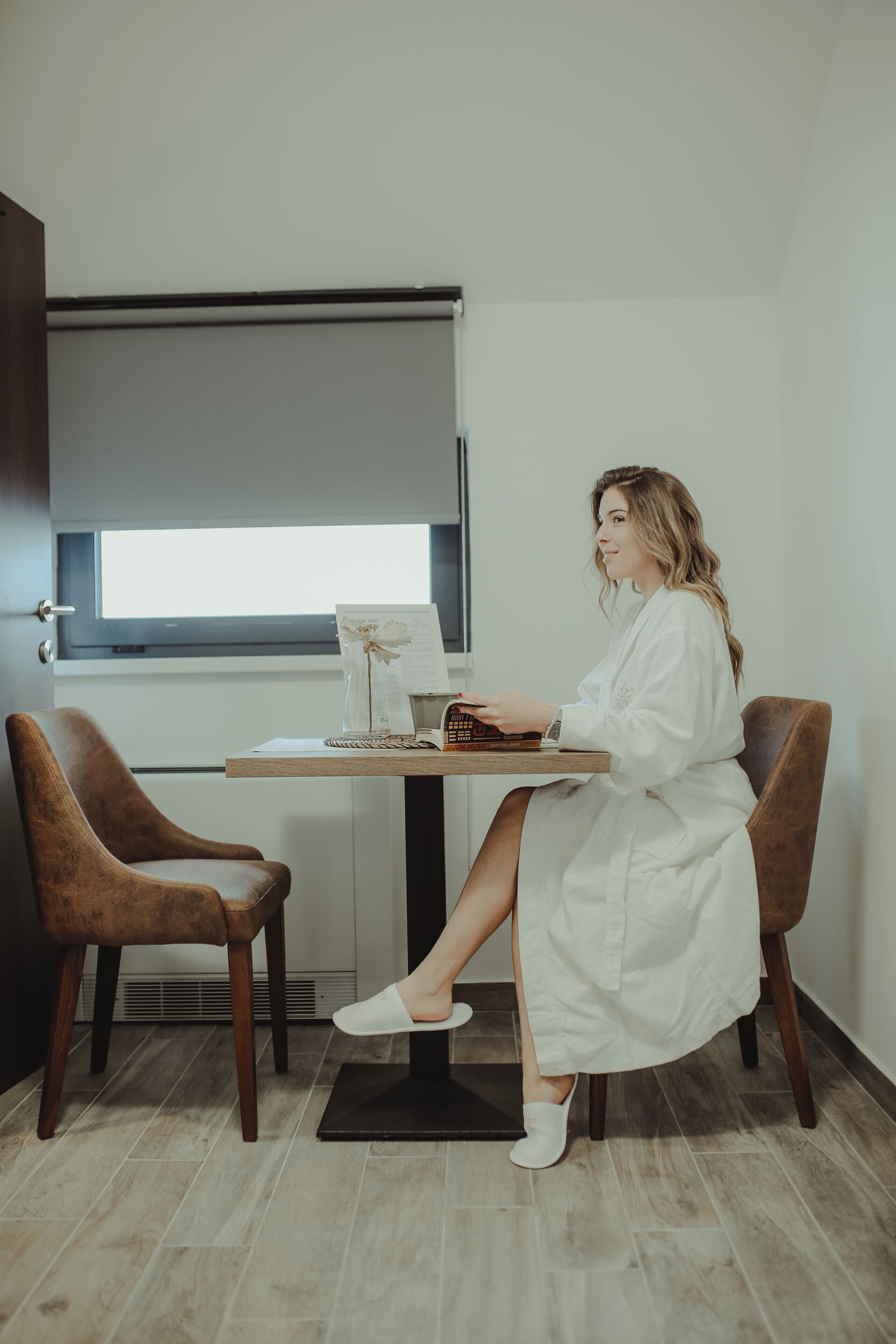A room with a wooden desk, two brown chairs, a window with blinds, and a white door.