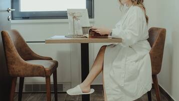 A room with a wooden desk, two brown chairs, a window with blinds, and a white door.