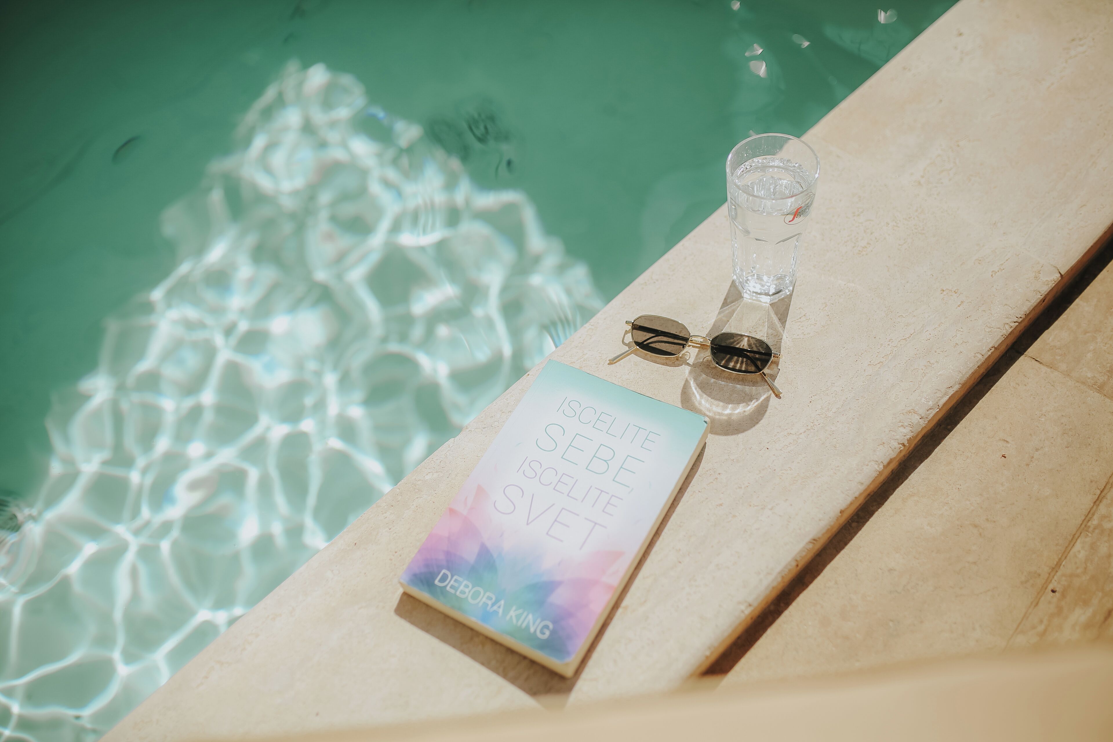 A book titled 'Iscelite Sebe Iscelite Svet' by Debora King placed on a poolside lounge chair.