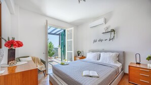 A modern bedroom with a bed, bedside tables, a desk, and a view of the outdoors. - J1 Holiday House Adjacent to Aphrodite Hills - Sea View (Kouklia)