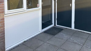 Ein Gebäudeeck mit einer weißen Tür, einem Fenster mit einer mattierten Glasscheibe und einer schwarzen Tür mit einem Spion.