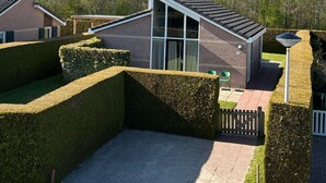 Ein modernes Haus mit einem geneigten Dach, großen Fenstern und einem gepflegten Garten mit Hecken.
