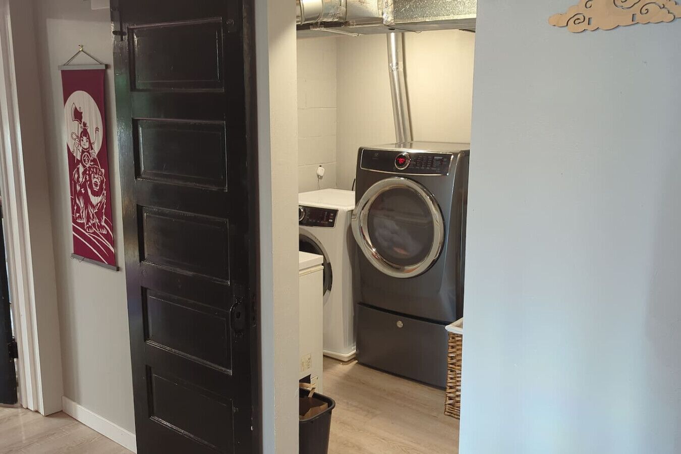 Une buanderie équipée d’un lave-linge et d’un sèche-linge, une porte ornée d’un panneau décoratif et un luminaire fixé au mur.