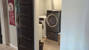A laundry room with a washing machine and dryer, a door with a decorative panel, and a wall-mounted light fixture.