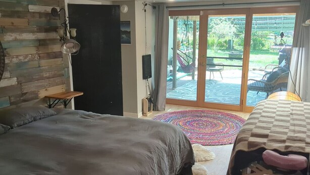 A bedroom with a bed, a small table, a chair, a rug, and a sliding glass door leading to an outdoor area.