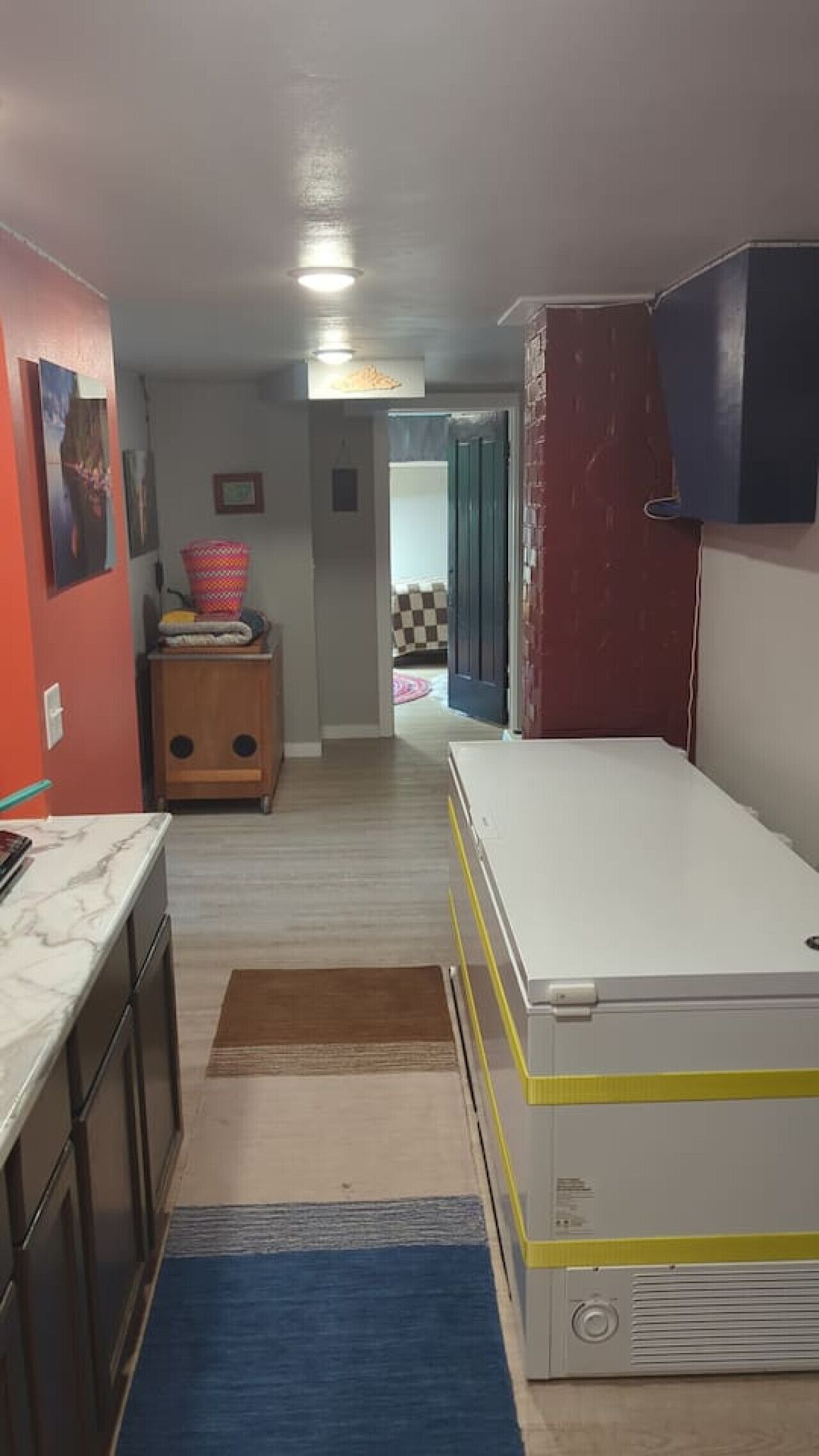 A narrow hallway with a kitchen area on the left, a white refrigerator on the right, and a door leading to another room.