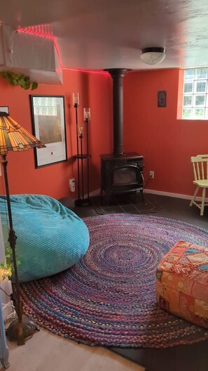 Um quarto com um grande puff, um tapete estampado, uma lareira e uma janela com vista.