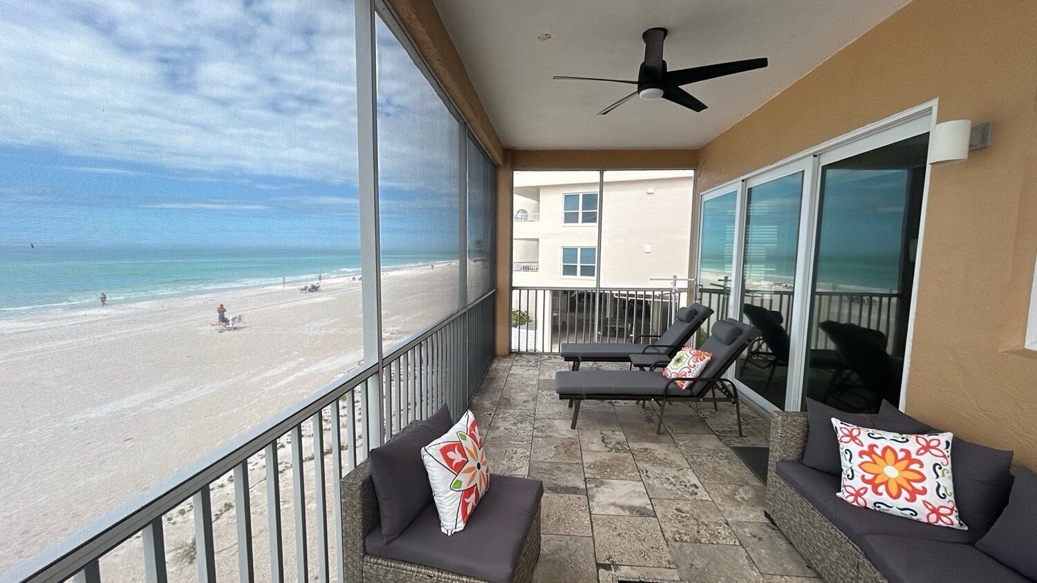 Ein Balkon mit Blick auf den Strand, ein Deckenventilator und zwei Liegestühle mit Kissen.