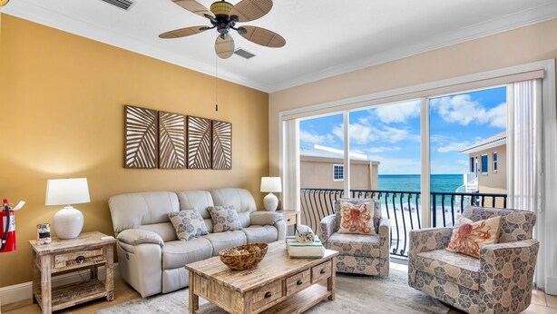 A living room with a sofa, armchairs, a coffee table, and a view of the ocean through large windows.