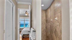 A bathroom with a shower, beige tiles, a towel rack, and a view of the ocean through a window.