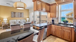 A kitchen with wooden cabinets, a black countertop, and a dining area with wicker chairs.