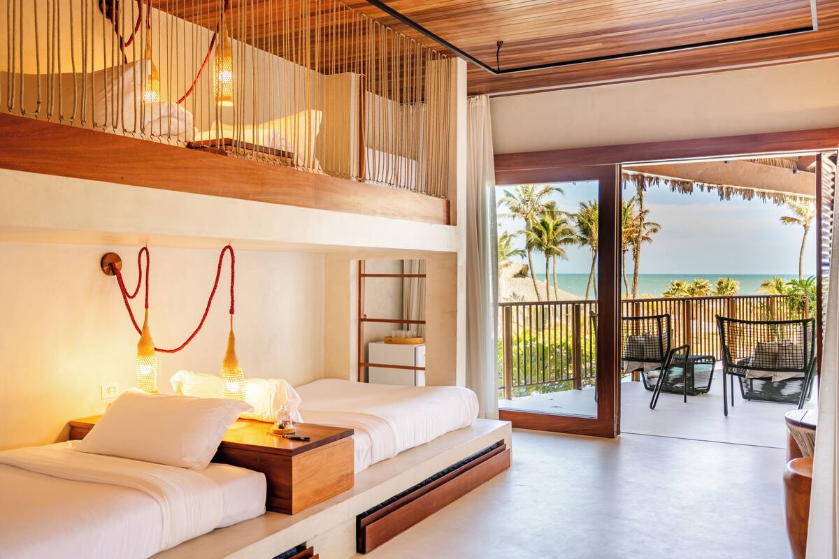 Una habitación de hotel moderna con balcón que da al mar, cama con ropa blanca y techo de madera.