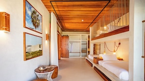 A hotel room with a wooden ceiling, a bed with white bedding, a nightstand, a small table with a candle, and a wall-mounted lamp. - Casa Siará - Preá (Cruz)